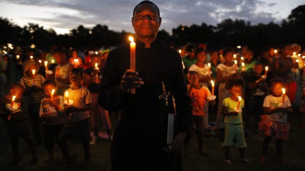A priest carries a candle with hundreds of people during a memorial for the late Nelson Mandela in Soweto, Johannesburg, South Africa, 4 December 2014.