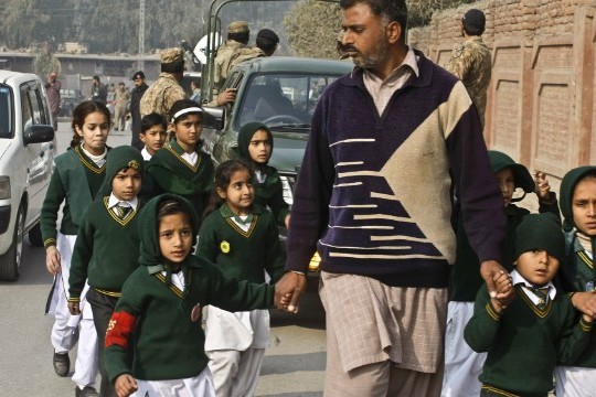 A man escorts students rescued from nearby school during a Taliban attack in Peshawar, Pakistan, Tuesday, Dec. 16, 2014. (AP Photo: Mohammad Sajjad)