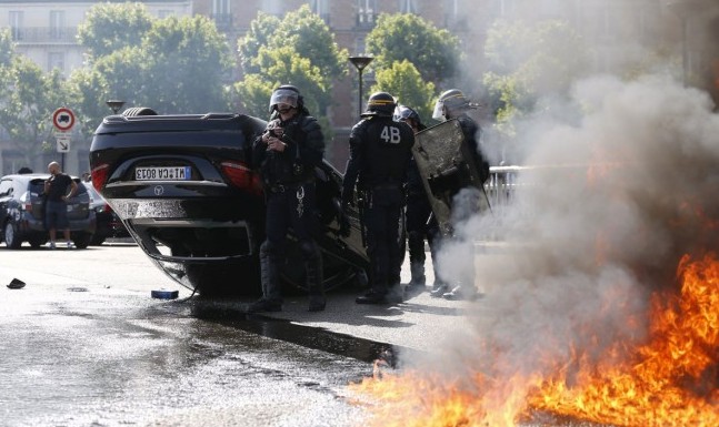 Riot police responded to protests in Paris after French taxi drivers overturned cars and set fire to tyres in protest against taxi app Uber