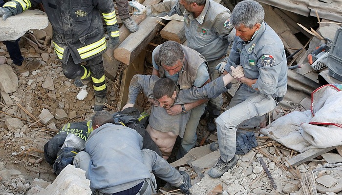 A dust-covered man trapped in the rubble of his home as he slept is pulled from a hole by rescuers in Amatrice this morning